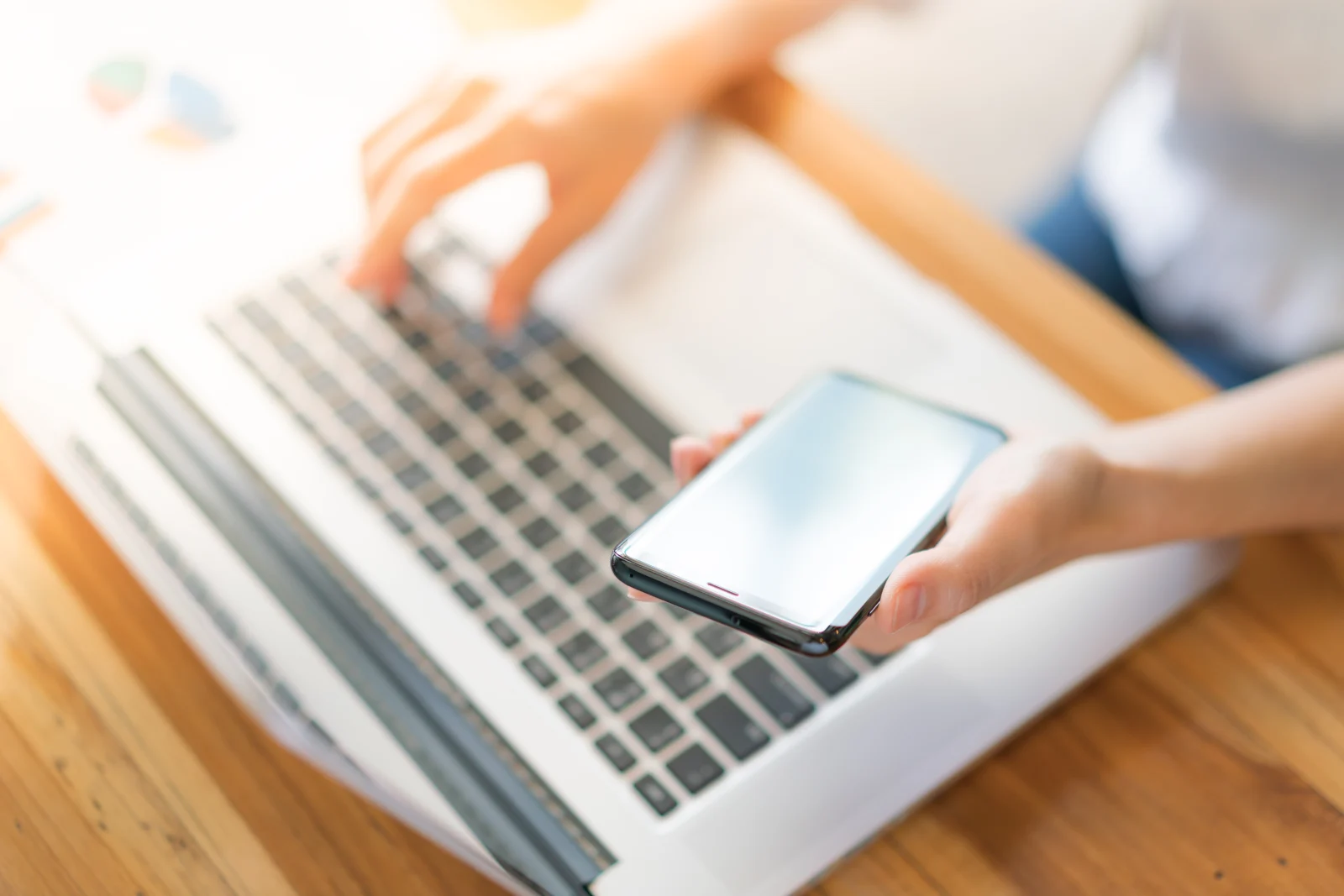 Osoba korzysta jednocześnie ze smartfona i laptopa przy biurku.